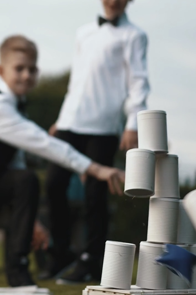 Boys in tuxedos laughing while knocking down cans with beanbags